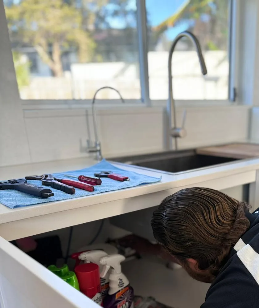 Plumber working under a kitchen sink with tools laid out